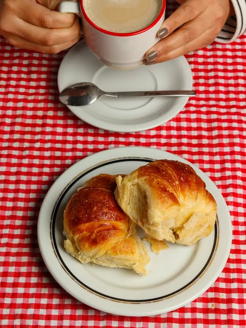 Café con leche y dos medialunas sobre un mantel a cuadros